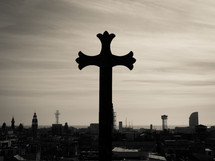 A gothic stone cross overlooking the sea-front city outlook, in black and white (b&w)