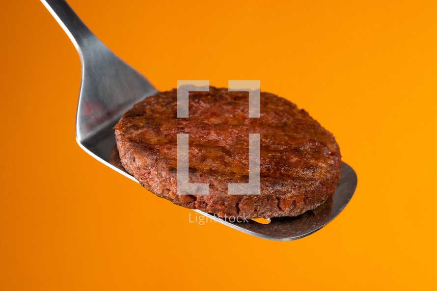 Meat steak on barbecue grilling tool - spatula handle. Cooking beef or pork patty. Raw cutlet for burger. Close-up photo. High quality photo