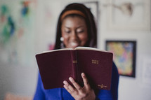 Smiling woman holding and reading a Bible.