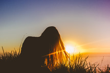 Silhouette of a woman sitting in the grass at daybreak.