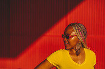 African-American woman standing in front of a red wall wearing sunglasses 