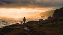 A woman walks with her dog along the trail down to the beach as the sun sets in the ocean. An epic view of a golden sunset, 