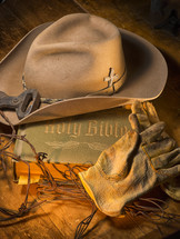 Cowboy hat and leather work gloves on top of a Bible.