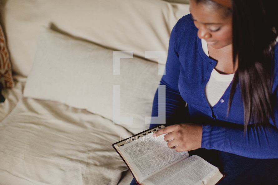 African-American woman reading a Bible on her bed 