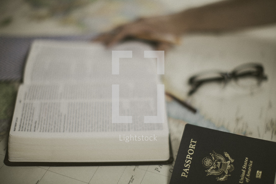 open Bible, passport, and reading glasses on a world map 