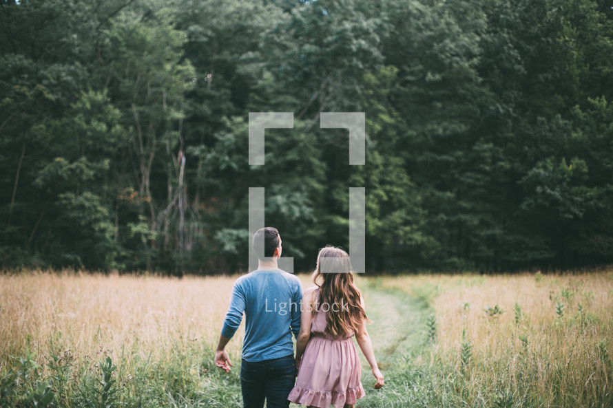 couple holding hands walking through a field 