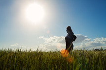 girl in a field on tall grass under bright sun