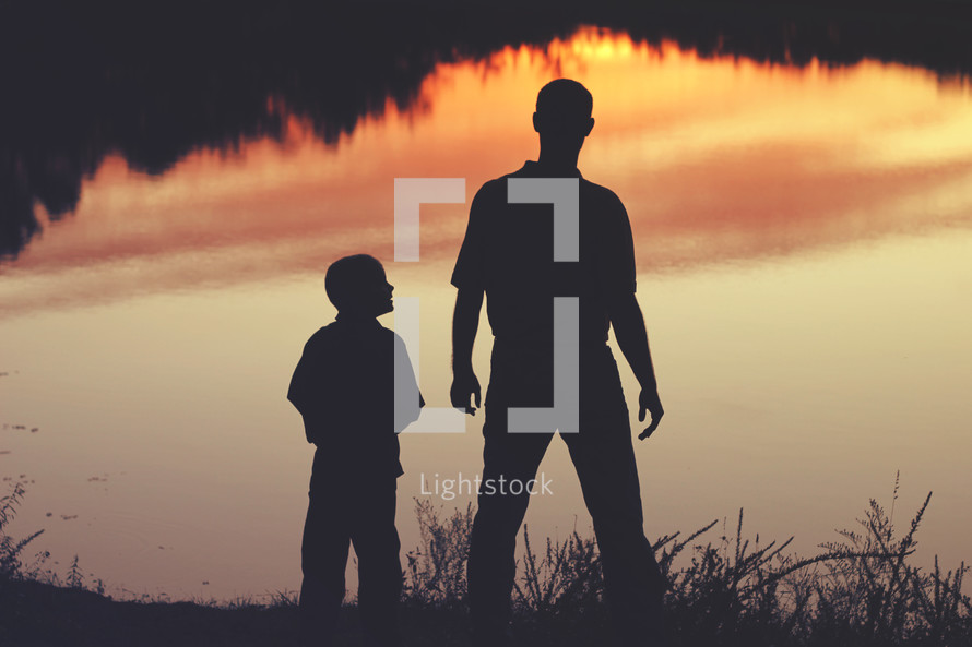 silhouette of a father and son standing by a lake 