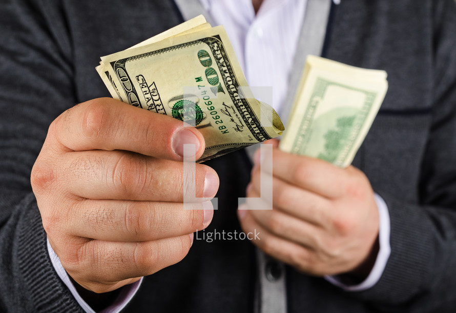 Hands holding a stack of hundred dollar bills, while offering folded hundred dollar bills.