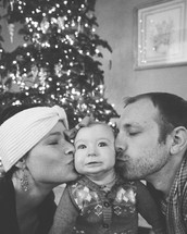 mother and father kissing their infant daughter at Christmas 