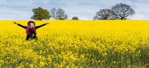 woman with outstretched arms standing in a field of wildflowers 