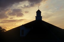 Steeple sunset - A building with a steeple and weather vein is silhouetted by a beautiful sunset just before dusk.