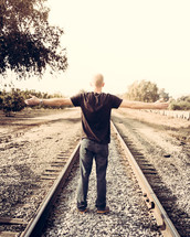 man with open arms on railroad tracks 