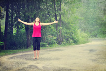 Woman walking outside in the rain with arms wide open.