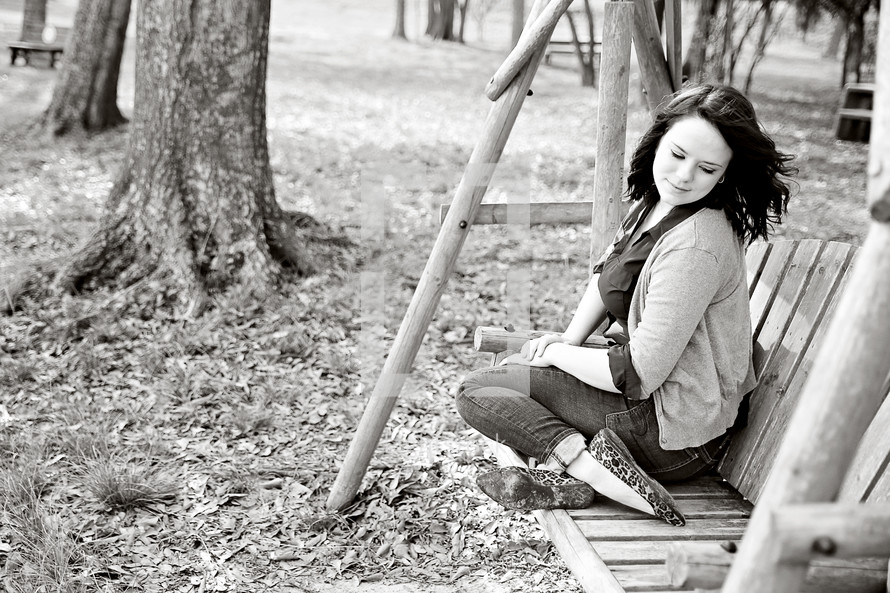 A young woman sitting outdoors on a wooden swing.