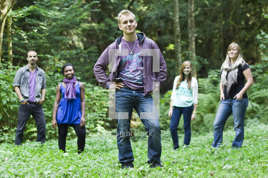 Young adults (church interns) in a forest field with their hands on their hips and in pockets.