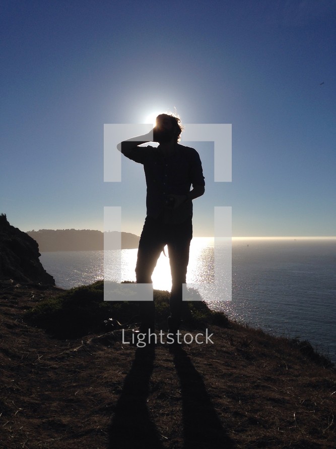 silhouette of a man standing at a lake shore under sunlight