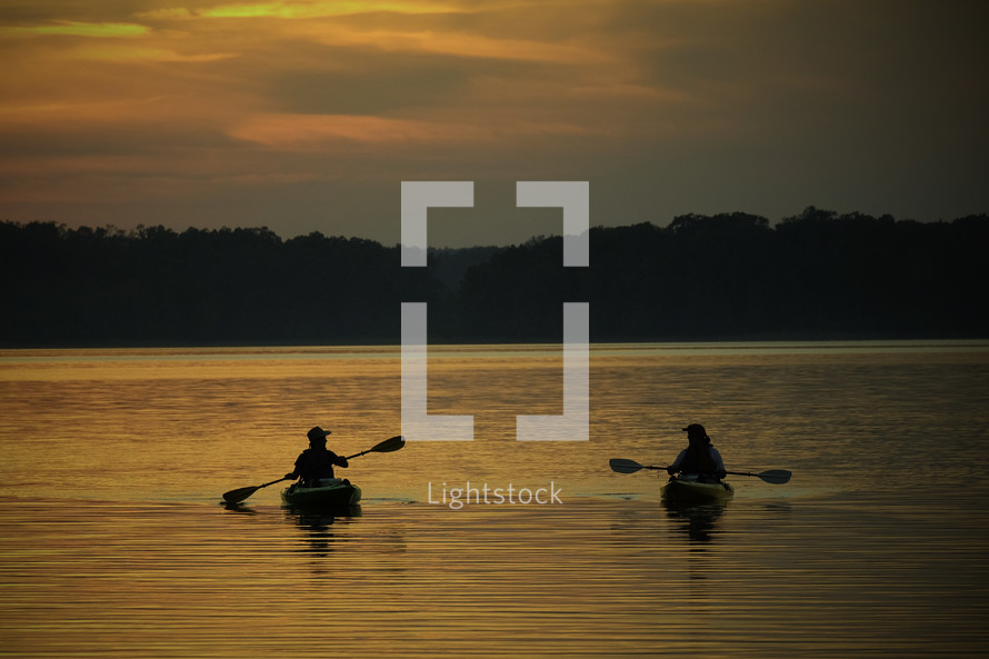 silhouettes of kayakers paddling at sunset 