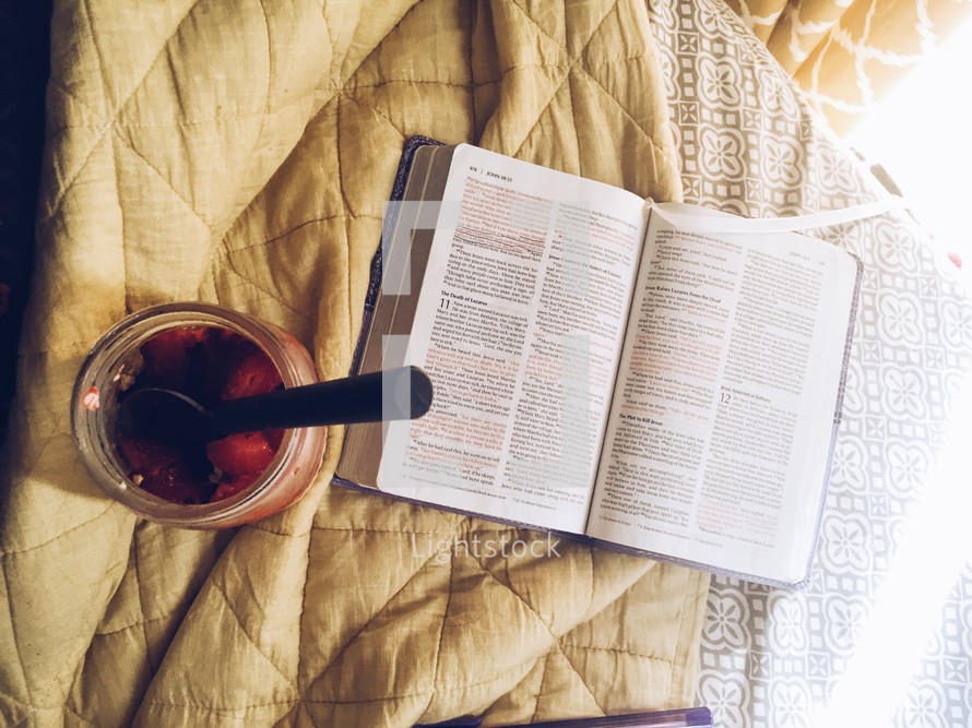 an open Bible on a bed and spoon in a jar 