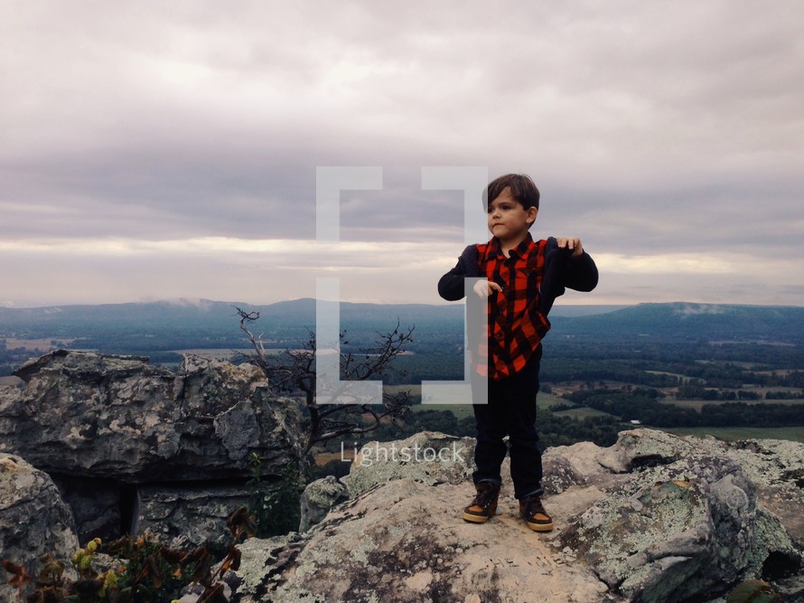 little boy standing at the top of a mountain 