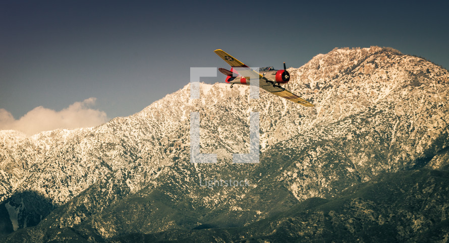 vintage single engine airplane flying over mountains 