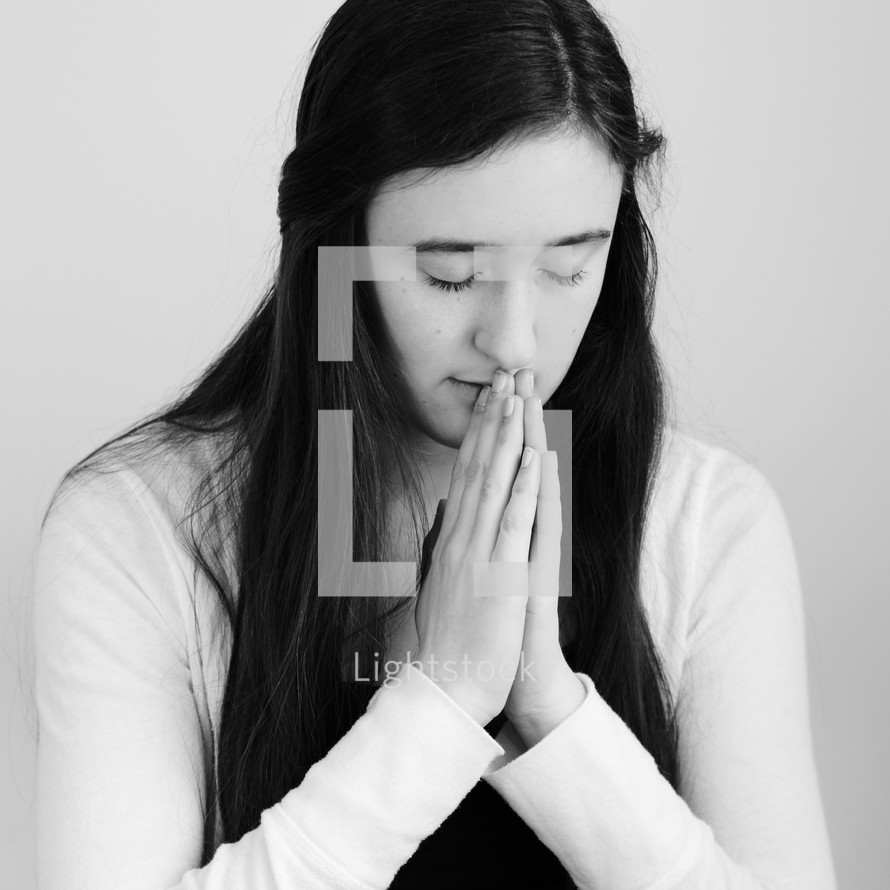 A young woman praying with hands folded.