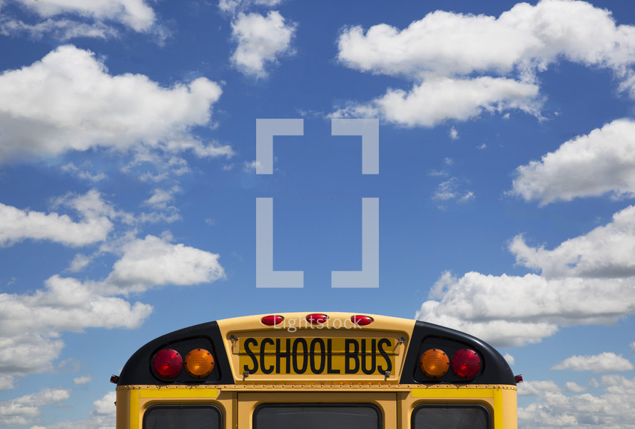The back of a school bus and a blue sky with clouds.