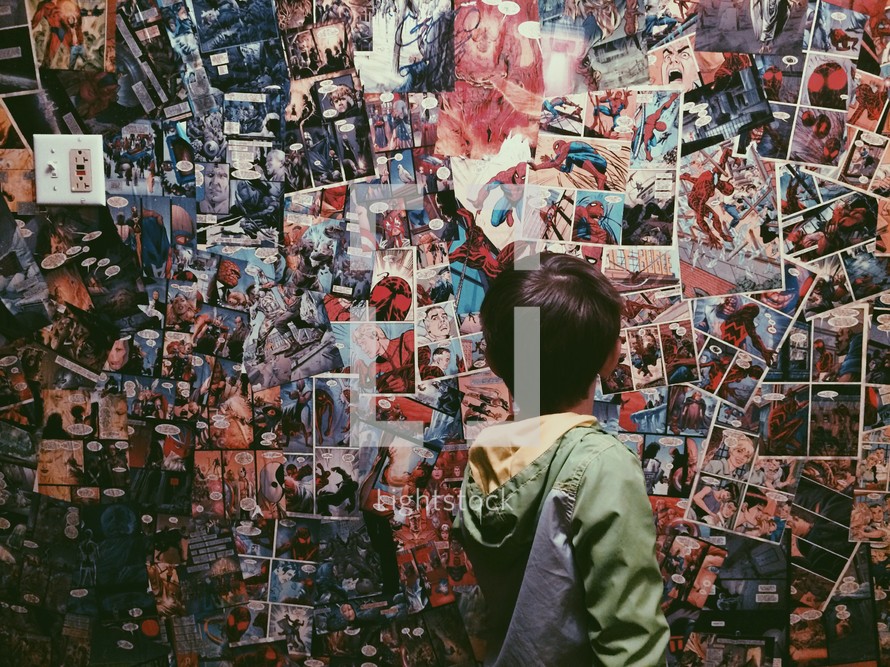 A boy looks at a wall covered in comic book pages.