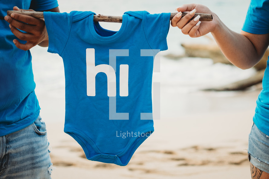 expecting couple holding up a onesie 