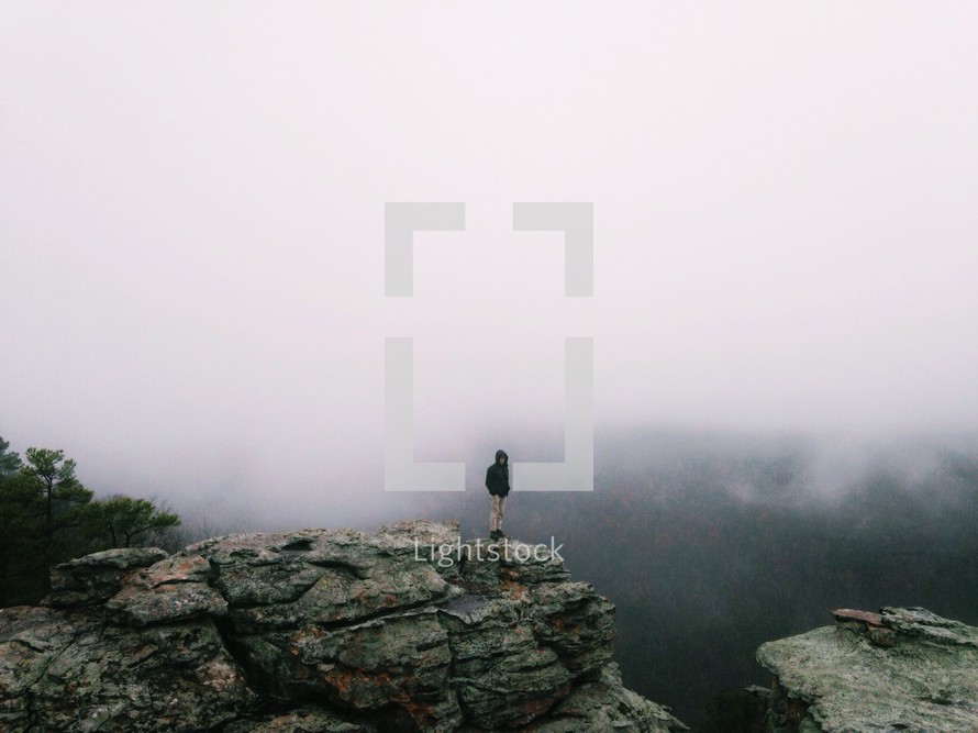 Man standing at the edge of a rocky cliff in the foggy haze.