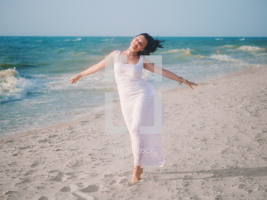 Gypsy young brunette Girl wearing white maxi long dress standing in the sea or ocean with waves and foam. Bohemian clothing style. Boho lifestyle