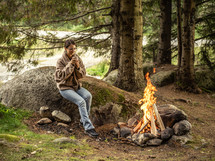 Woman sitting by campfire in a forest