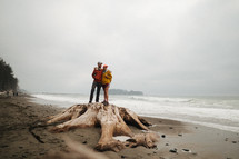 couple standing on driftwood on a beach 