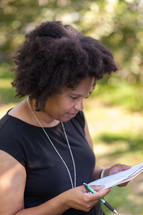 An African American woman reading and holding a pen outdoors 