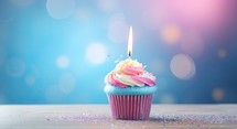 Cupcake with candle on blue bokeh background. Birthday concept