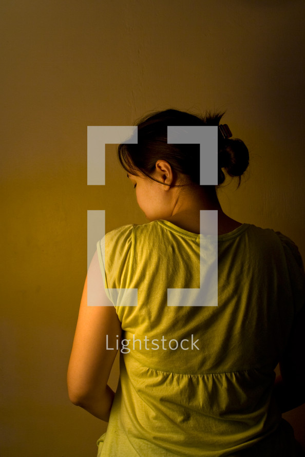 View of woman from behind with partial view of face. Low key image depicting sadness, depression, or loneliness.