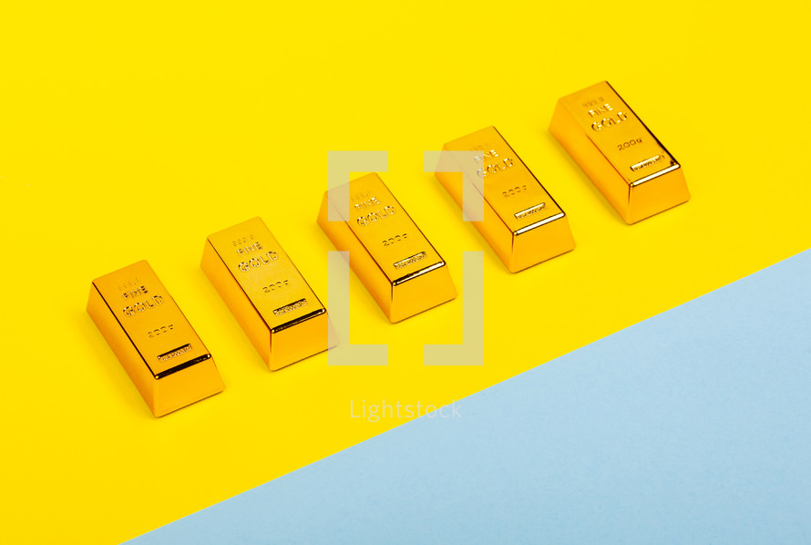 Bars of gold bullion on yellow and light blue background. Financial concept.