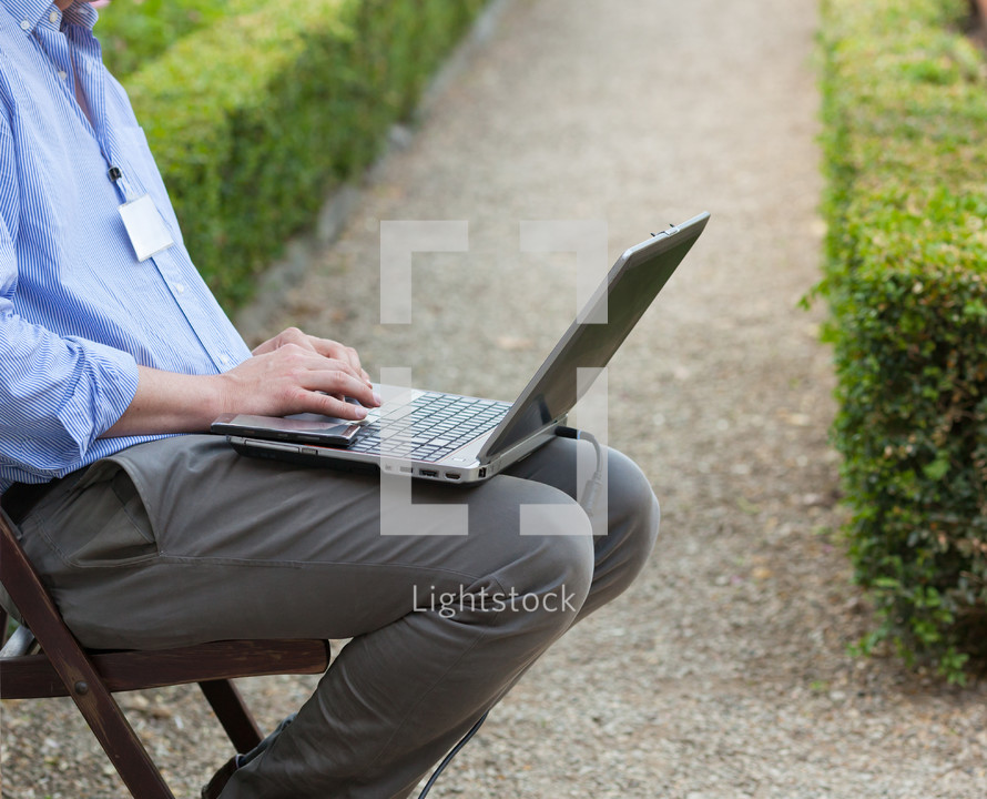 Businessman holding a laptop on his knees and looking at the laptop while sitting outdoors.