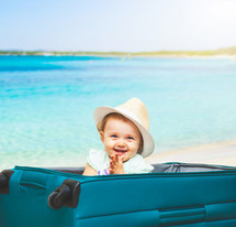 Baby girl sitting in suitcase on the sand of the beach with sea background