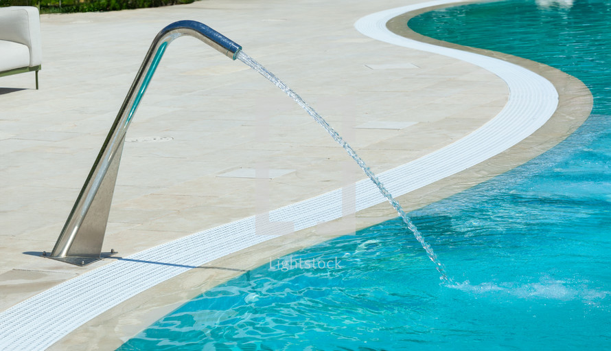 Refreshing waterfall cascades into the turquoise water of a luxury resort swimming pool