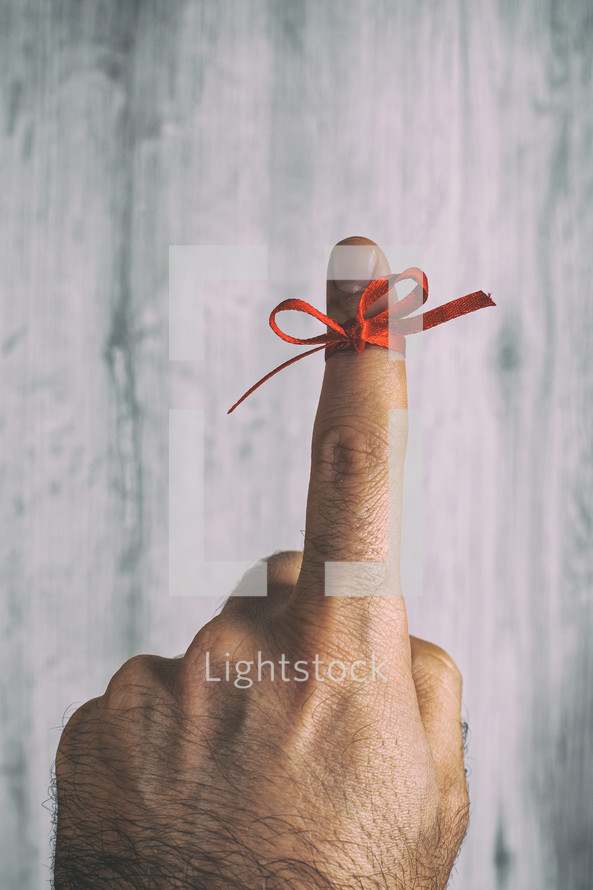 Man is showing his finger with a red ribbon tied around it, serving as a visual reminder