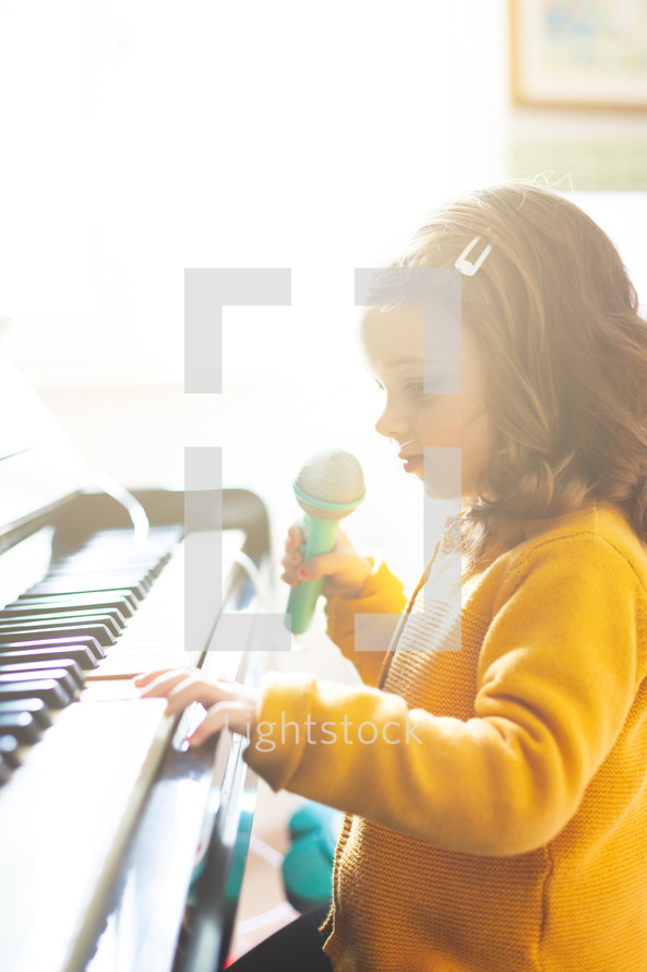 Girl toddler plays the piano and sings with the toy microphone