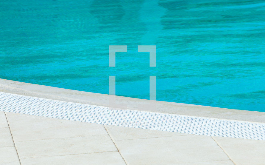 Turquoise water in an outdoor swimming pool is glittering on a sunny day, nobody is around