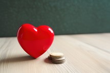 Red heart and coins on wooden table. Valentine's day concept.