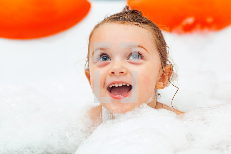 Happy little girl takes a bath in a hydromassage bathtub with foam.