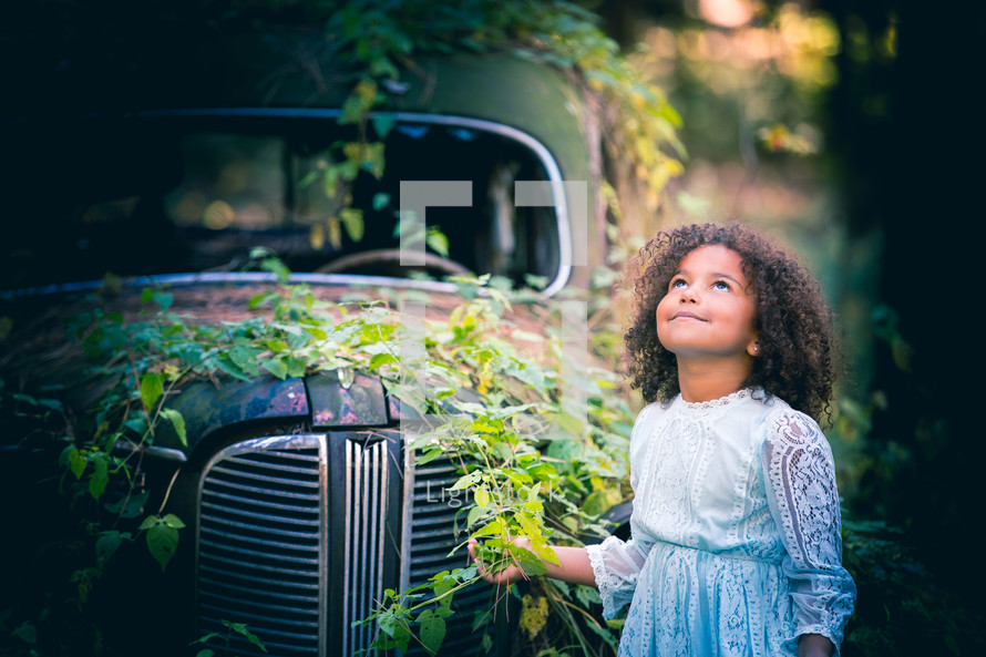 a little girl standing in front of a vintage car covering in ivy 