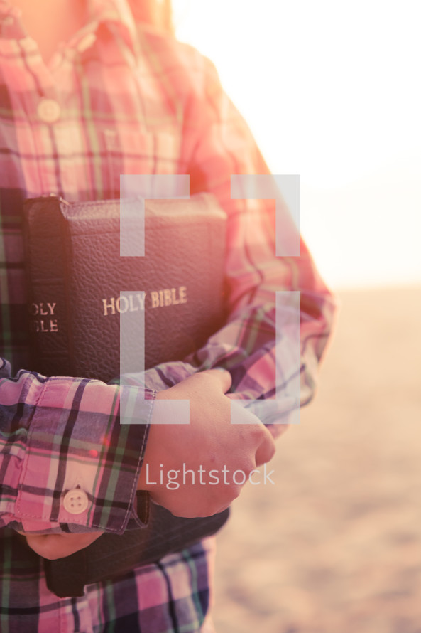 young girl standing on the beach holding her bible at sunset