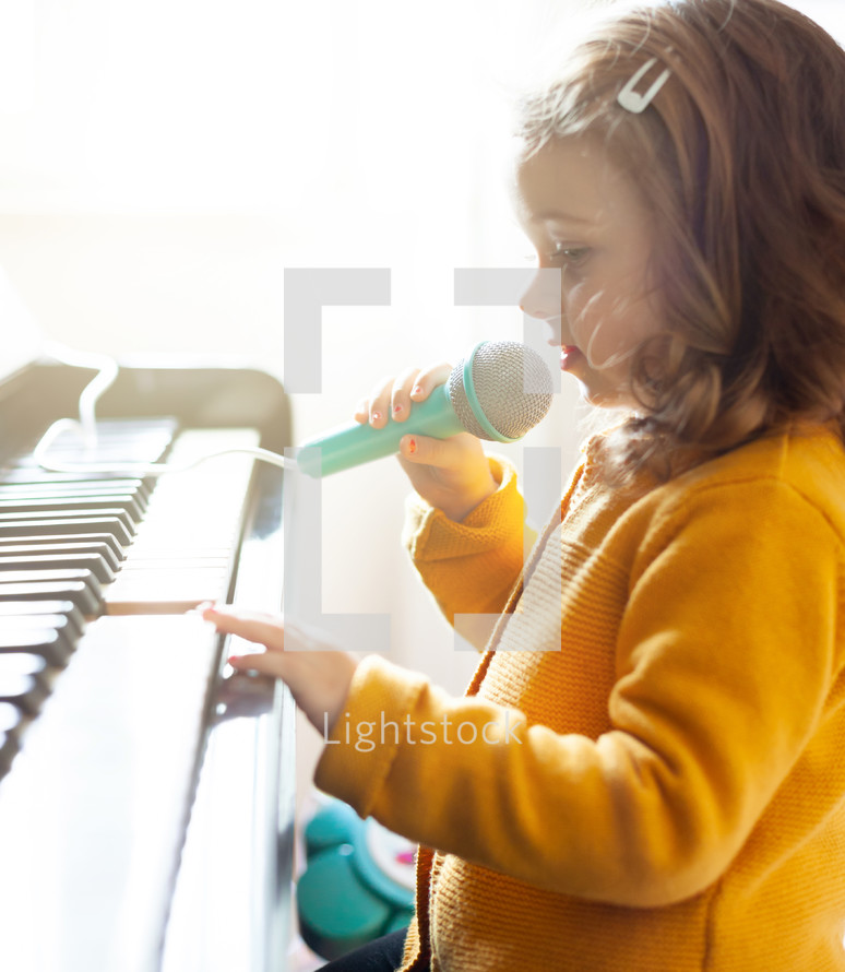 Girl toddler plays the piano and sings with the toy microphone.
