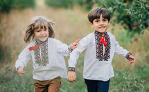 Little ukrainian boys cheerfully running along path in apple garden lawn. Children together in traditional embroidery vyshyvanka shirts. Ukraine, brothers, freedom, national costume, patriots.
