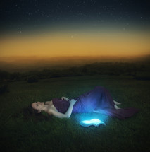 woman lying in the grass and an open Bible glowing 